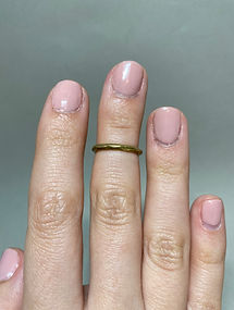 Close-up of a hand with pink nails wearing a hammered brass ring on the middle finger.