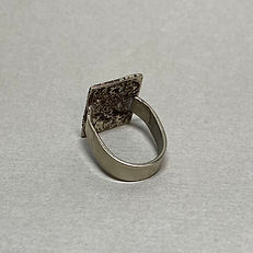 Side view of a silver ring with a rectangular textured face and a wide band on grey background.