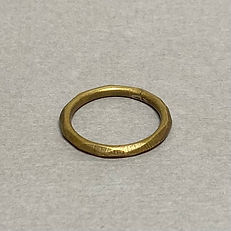 Flat-lay of a textured brass ring with a hand-forged, faceted surface on a gray background.