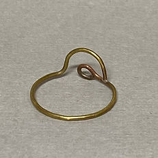 Brass ring with a wavy peak and looped end, shown on a gray surface with visible solder point.