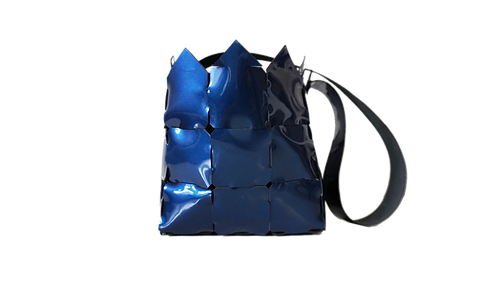 Glossy navy blue woven handbag with pointed top edges and a long strap, shown on a transparent background.