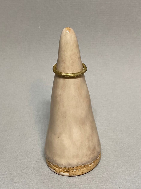 Simple brass ring with a hammered texture displayed on a ceramic cone stand against a gray background.