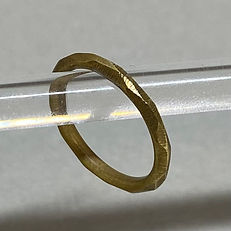Brass ring with a faceted surface resting on a clear acrylic rod, shown in close-up.