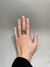 Hand wearing a silver ring with a wide, textured rectangular face on the middle finger against grey background.
