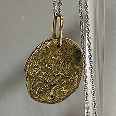 Close-up of textured circular gold pendant on a silver chain.