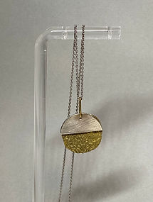 Round pendant necklace with silver top and textured gold bottom on a display stand.