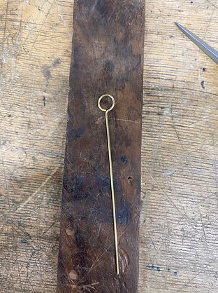 Brass wire bent into a loop placed on a dark wooden block on a jewelry workbench.