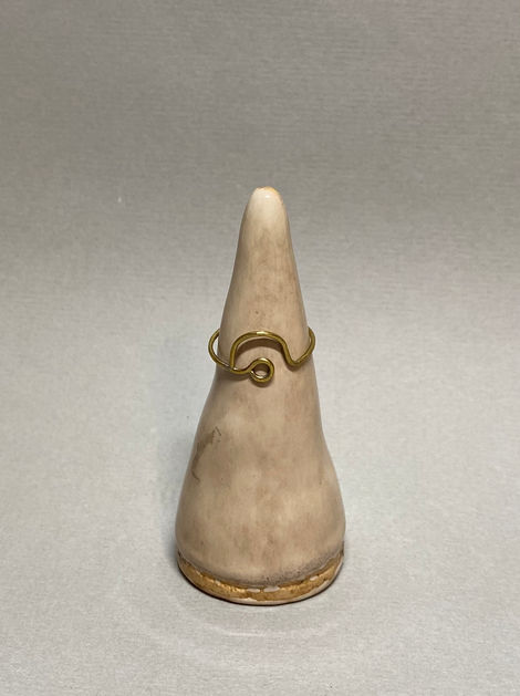 Brass ring with a single loop and wave detail displayed on a ceramic cone stand against a gray background.