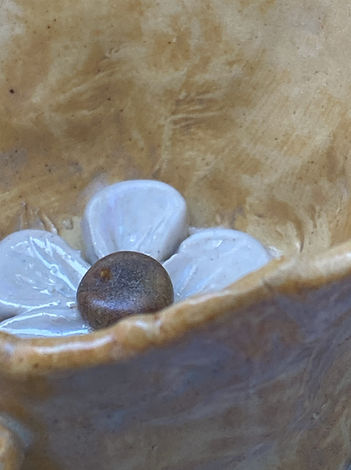 Close-up of a yellow ceramic cup’s interior, highlighting a raised white flower with a brown center at the bottom.