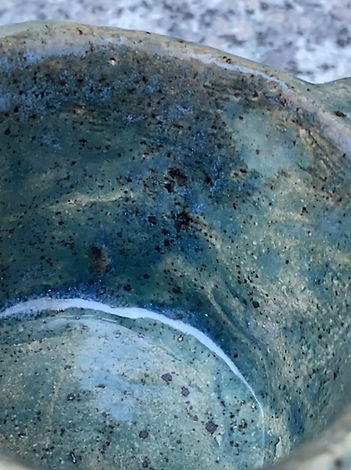 Close-up of a green ceramic cup’s interior, showing textured glaze with dark speckles and a curved white streak.