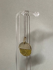 Side view of silver and gold round pendant necklace hanging on a clear acrylic display.