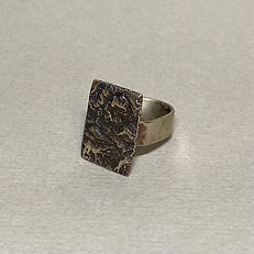 Textured rectangular metal ring with a wide band placed on a grey surface.