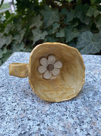 Top view of a yellow ceramic cup with a sculpted flower at the bottom, resting on a granite surface with leafy background.