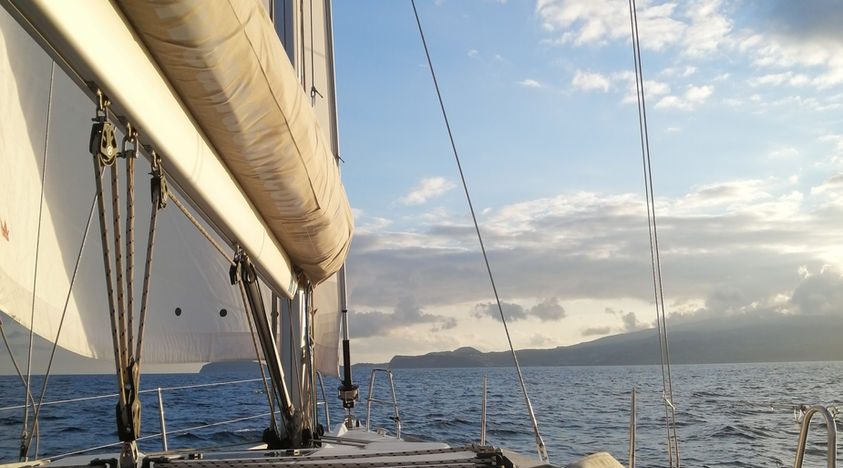 Sailboat deck view of ocean and distant mountains.