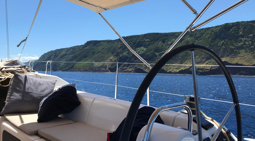 Boat deck with steering wheel overlooking a green coastline