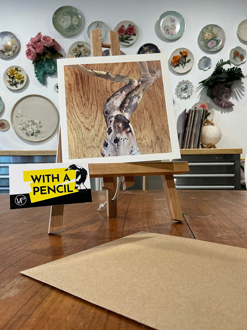 Gift card reproduction of the "Myall Street" tree painting. The original painting is on uncoated plywood, the tree is a grey and dark barked gum tree that is focussing on the double trunk that resembles a reclining nude female. There are no leaves.