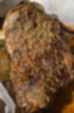 Close-up of a roast seasoned with herbs, golden-brown and juicy, resting in a dish with oily juices beneath, creating a savory and appetizing mood.