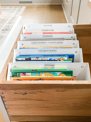 Drawer with dividers labeled Plain Paper, Notebooks, Stickers, and more. Organized office cabinet on a light wooden floor. Cozy setting.