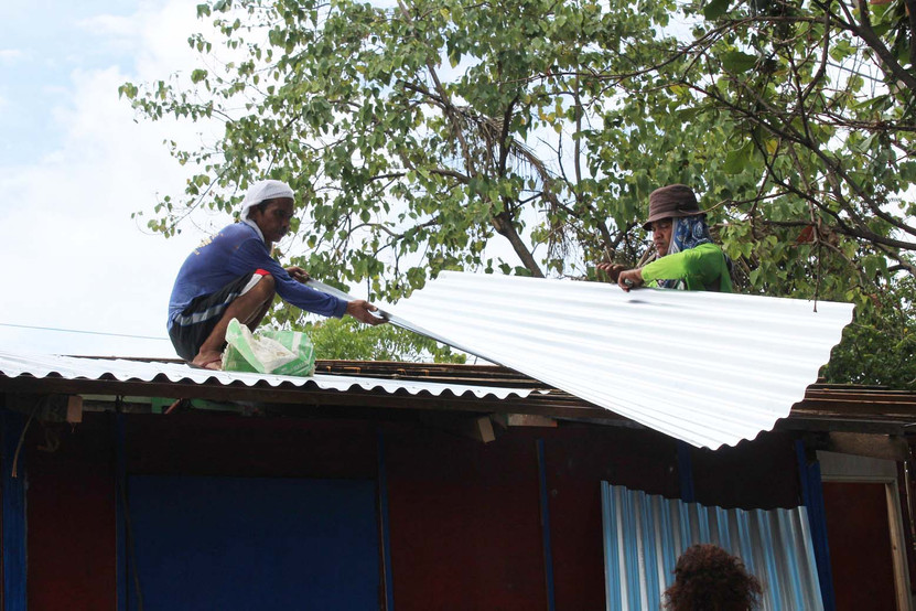A two construction workers replacing the old roof with a new GI sheet
