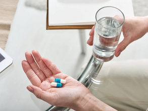 Una persona sosteniendo pastillas y un vaso con agua.