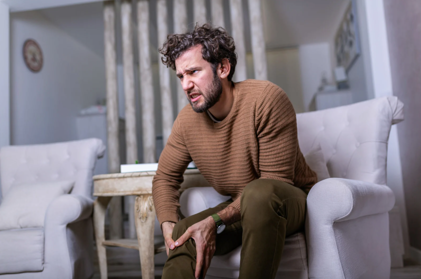 Hombre adulto tocándose la rodilla en señal de dolor.