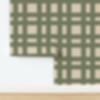 Green and beige plaid-patterned wallpaper partially unrolled against a white wall and wooden floor. No text or people present.