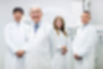 Four smiling medical professionals in white coats, posing in a medical office.