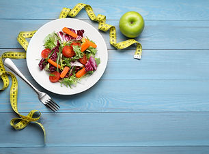 Plate of fresh vegetable salad, apple and measuring tape on light blue wooden table, flat
