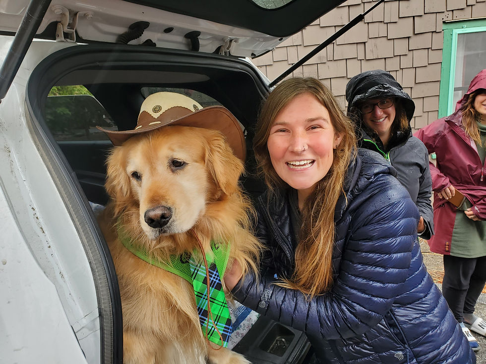 The author smiles and poses with a golden retriever who is wearing a green tie and little cowboy hat and sits in the back of his very own car.