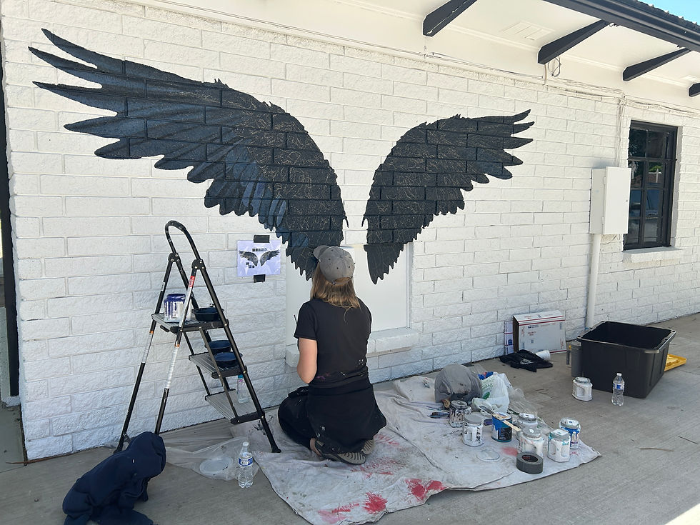 an artist paints raven wings on a white brick wall