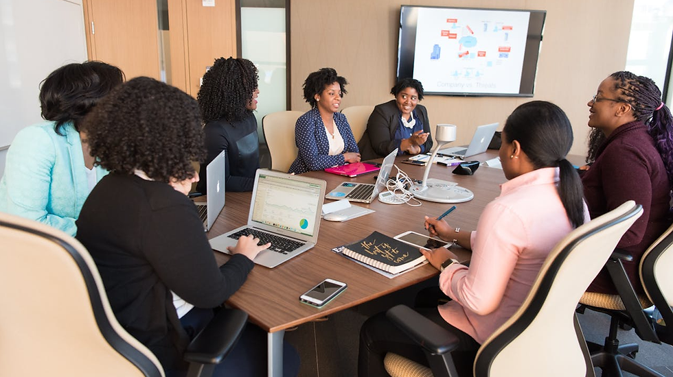Descrição da Imagem: Sala de reunião composta por 07 mulheres negras sentadas trabalhando ao seu redor (Foto: Christina Morillo).