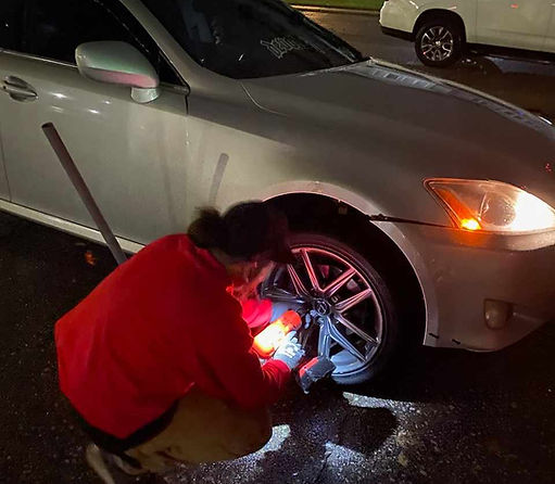 Roadside assistance technician changing a flat tire on a car. 