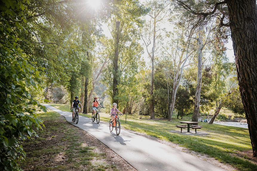 Happy family cycling together along the scenic Ovens River bike path in Bright, Victoria – enjoying a sunny ride through the stunning High Country landscape