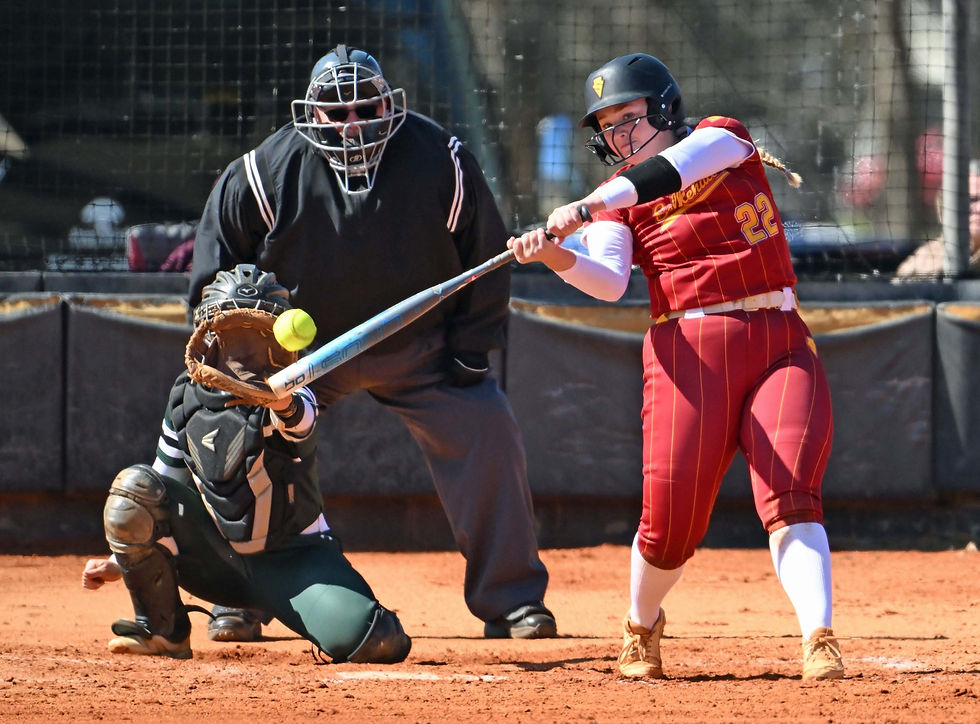 Softball game action: batter in red uniform hitting a yellow ball, catcher ready, and umpire observing. Sunny day on a dirt field.