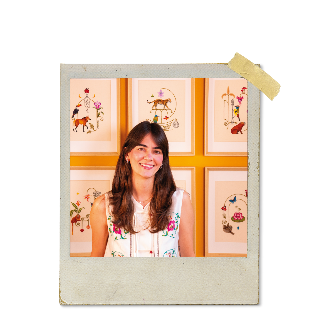 Ayeska sorrindo posando em frente a desenhos florais e coloridos no fundo.