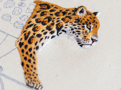 Detalhe de bordado de onça pintada em tecido creme. Ayeska.