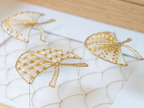 Três enfeites folha dourados, sobre uma superfície branca, em exibição. Detalhes.