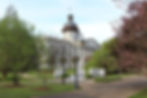 Historic building with a domed roof and columns, flanked by spring trees and lampposts. Pathways and vibrant pink blossoms set a tranquil mood.