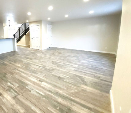 Spacious living room with wood-look flooring, showing stairs and a kitchen area.