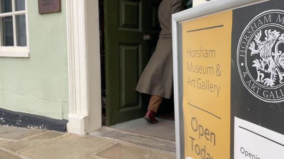 Luna is seen walking through the door of the museum, with the museum sign in the foreground.