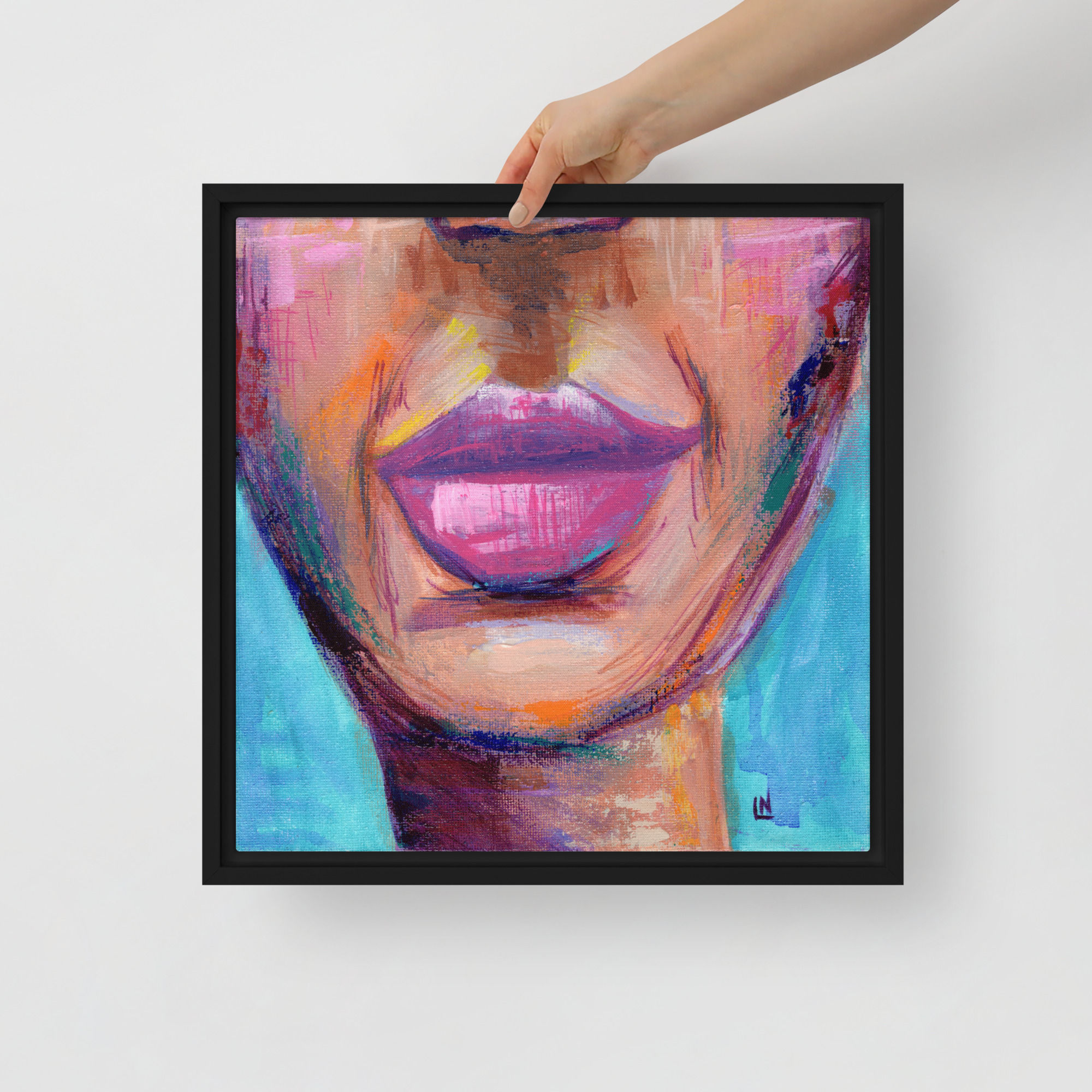 A hand holding a framed (black) canvas print of mhm. (smirk against turquoise background).