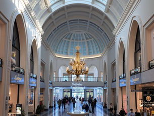 The picture shows a commercial area with lined up stores and people shopping. 