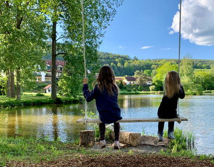 Zwei Mädchen schaukeln am See, Seehotel Gut Dürnhof im Hintergrund
