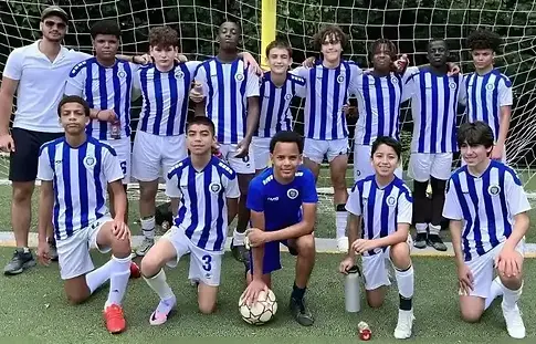 A youth travel soccer team from Bronx, NY, poses proudly on the field after a match in a local park on a sunny afternoon with Alba FC.