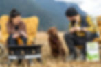 Couple camping with dog around campfire, featuring Red Dog Blue Kat Everyday Raw Anywhere gently dried raw dog food