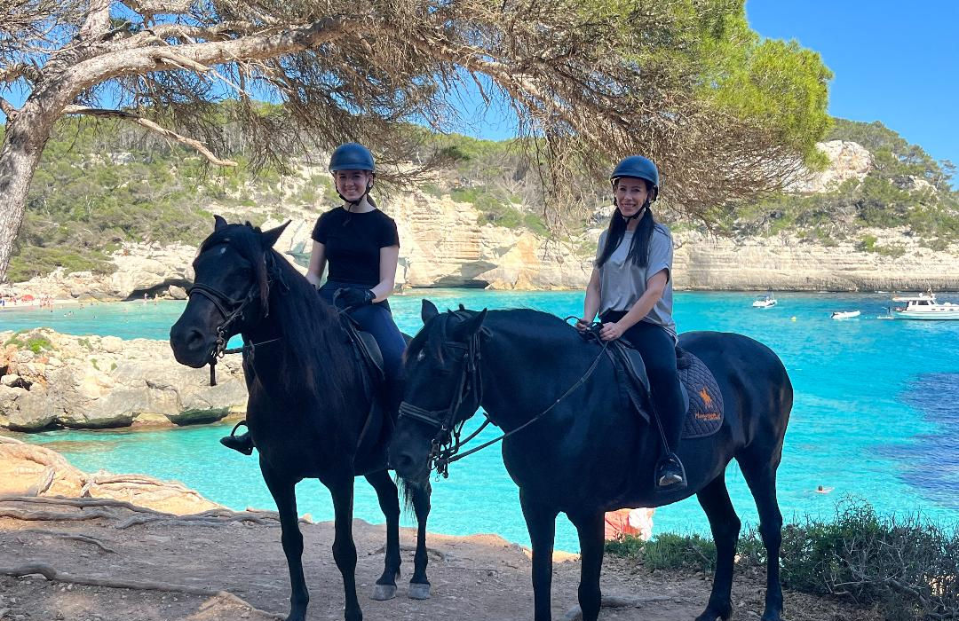 Two women riding black horses at the coast.