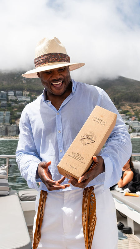 Seabelo Senatla sailing on the Mirage in Cape Town holding a bottle of 2 cultivar white wine by Glory.