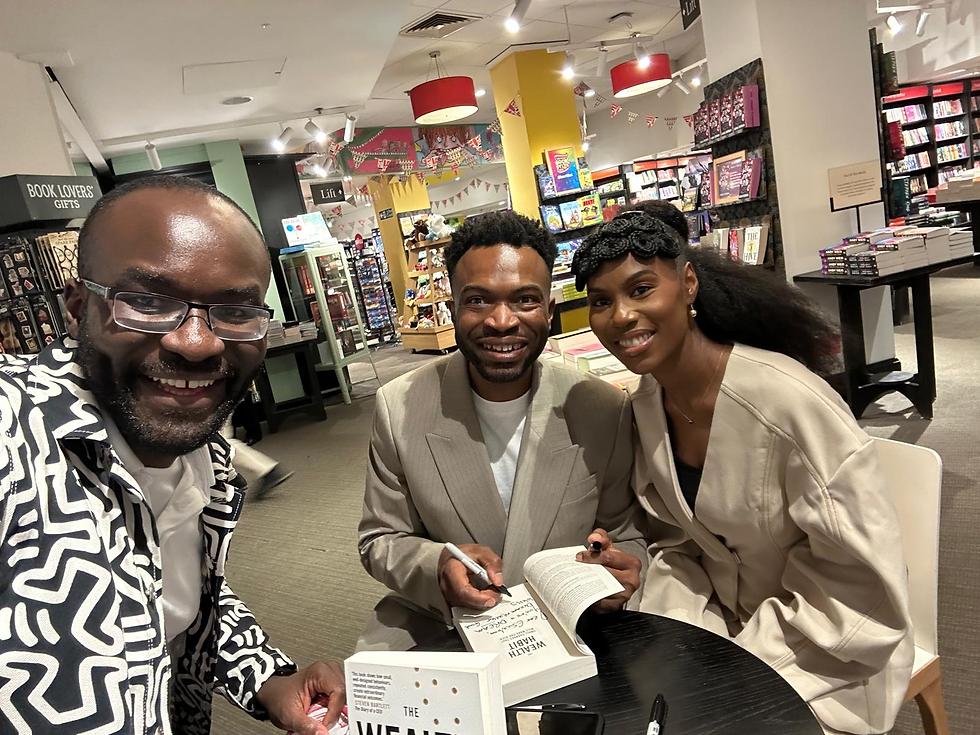 The Wealth Habit Book Launch with Ken & Mary Okoroafor. Three people smiling in a bookstore, one holding a signed book. Bookshelves and colorful decor in the background create a lively atmosphere.