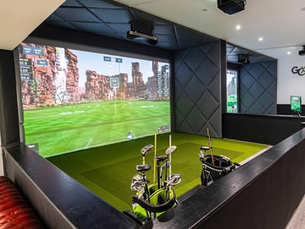 High-resolution view of a modern indoor X-Golf simulator bay equipped with golf clubs and screen tracking technology.