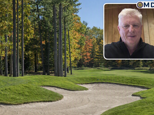 A landscape photograph of a sand bunker in the foreground, bordered by a green fairway and tall pine trees with autumn foliage, featuring an inset video box in the upper right showing General Manager Steve Zimmerla in a black quarter-zip against a wood-paneled wall with the MDG logo.